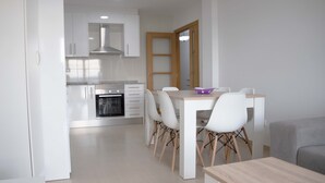 A modern kitchen with white cabinets, a built-in oven, and a dining area with a wooden table and white chairs. - APARTAMENTOS TERRAMAR BOIRO With sea views in the Ría de Arousa (Galicia) (Boiro)