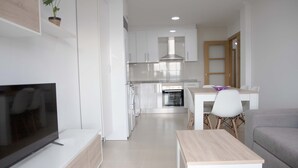 A modern kitchen with white cabinets, a built-in oven, and a dining area with a table and chairs. - APARTAMENTOS TERRAMAR BOIRO With sea views in the Ría de Arousa (Galicia) (Boiro)