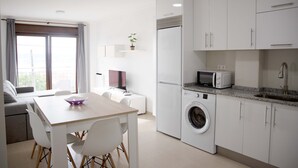 A modern kitchen with white cabinets, a washing machine, a microwave, and a dining area with a table and chairs. - APARTAMENTOS TERRAMAR BOIRO With sea views in the Ría de Arousa (Galicia) (Boiro)