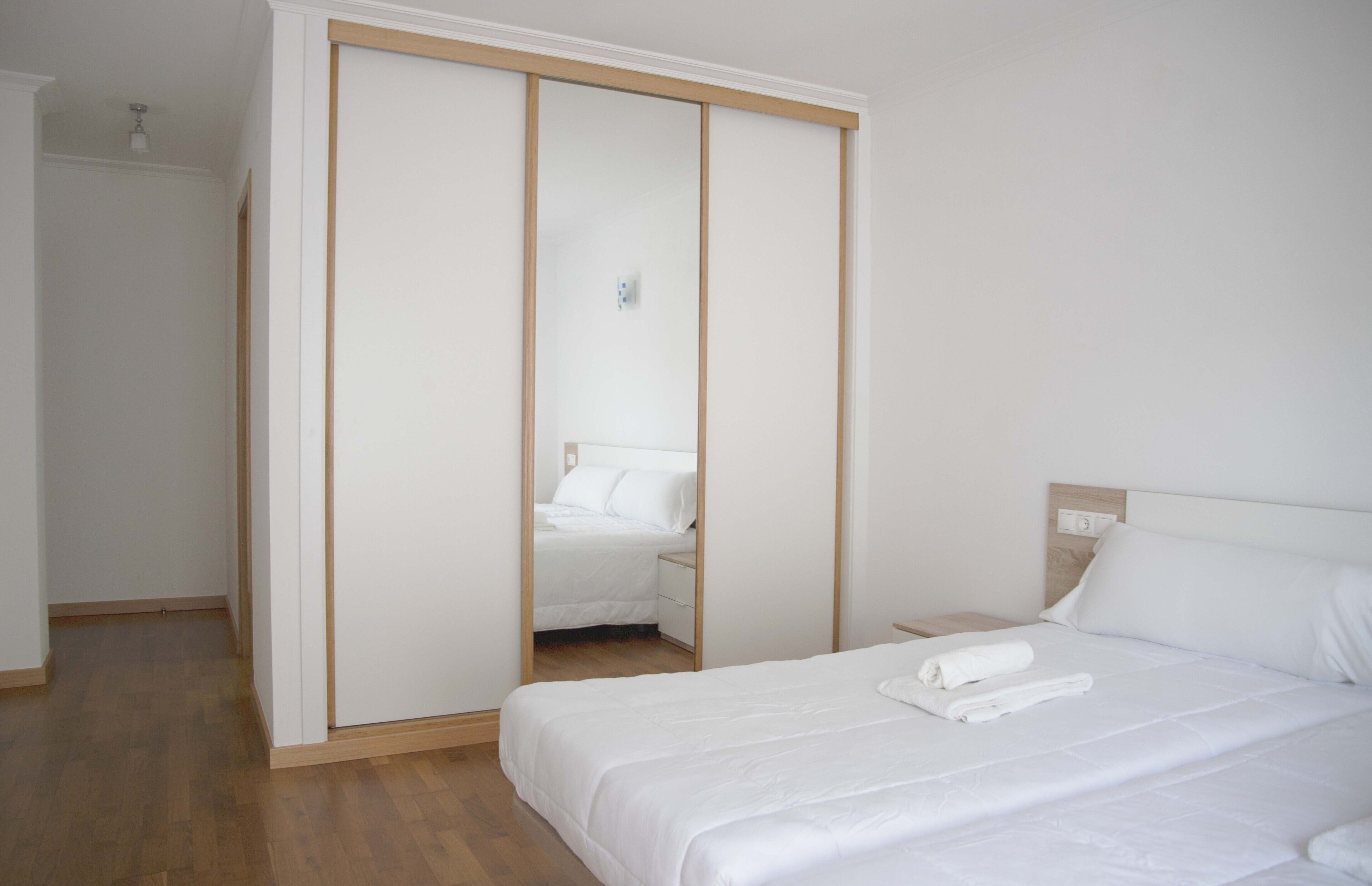 A bedroom with a bed, a wooden nightstand, a white wardrobe, and a mirror.