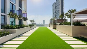 A modern building with a green artificial turf pathway, white stepping stones, and surrounding greenery.