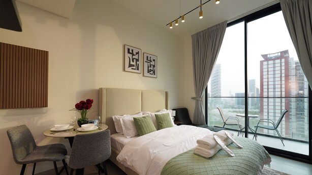 A modern hotel room with a large bed, a dining area with a table and chairs, and a balcony with a city view.