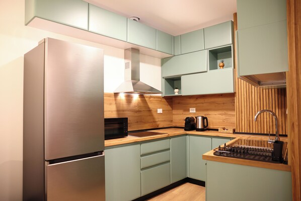 A modern kitchen with light green cabinets, a stainless steel refrigerator, a wooden countertop, and a built-in sink.