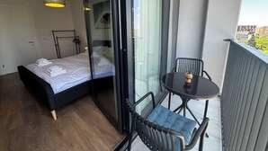 Un dormitorio moderno con cama, puerta de cristal que da a un balcón, una mesita y una silla.