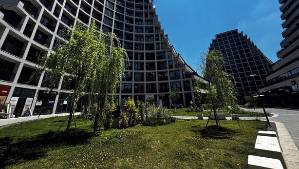 Un moderno edificio de gran altura con fachada de entramado, rodeado de césped y árboles bien cuidados.