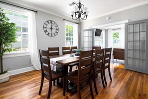 A dining room with a wooden table and chairs, a clock on the wall, and a potted plant.