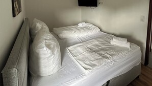 Ein Einzelbett mit weißer Bettwäsche, ein wandmontierter Flachbildfernseher und eine Deckenleuchte.