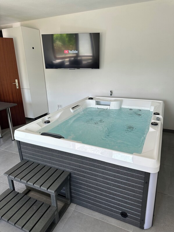 A modern bathroom with a freestanding bathtub, a mounted television, and a wooden bench. - Quiet vacation apartment with a hot tub and barrel sauna (Medebach)