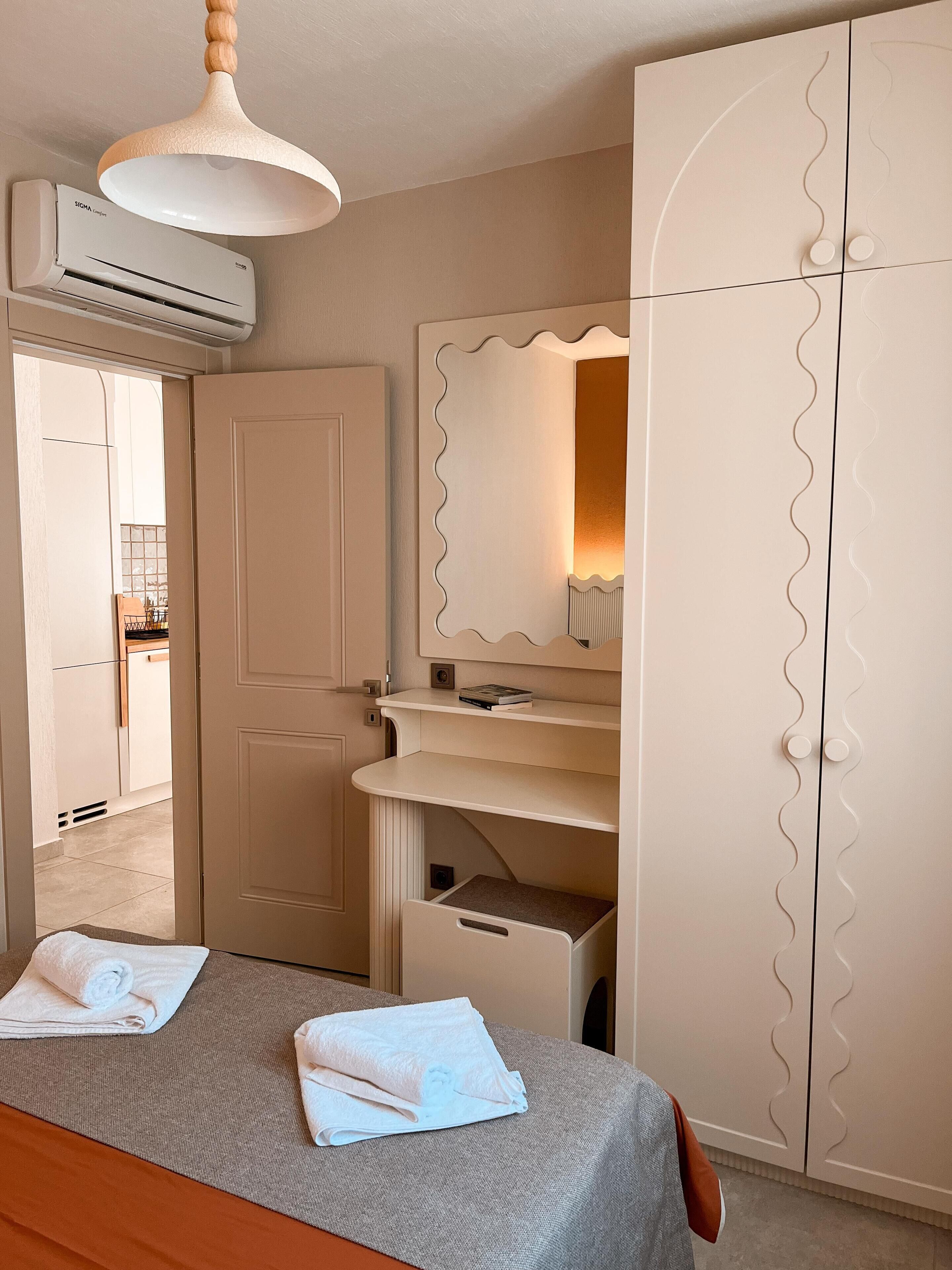 A bedroom with a bed, a bedside table, a wardrobe, a mirror, and an air conditioning unit.