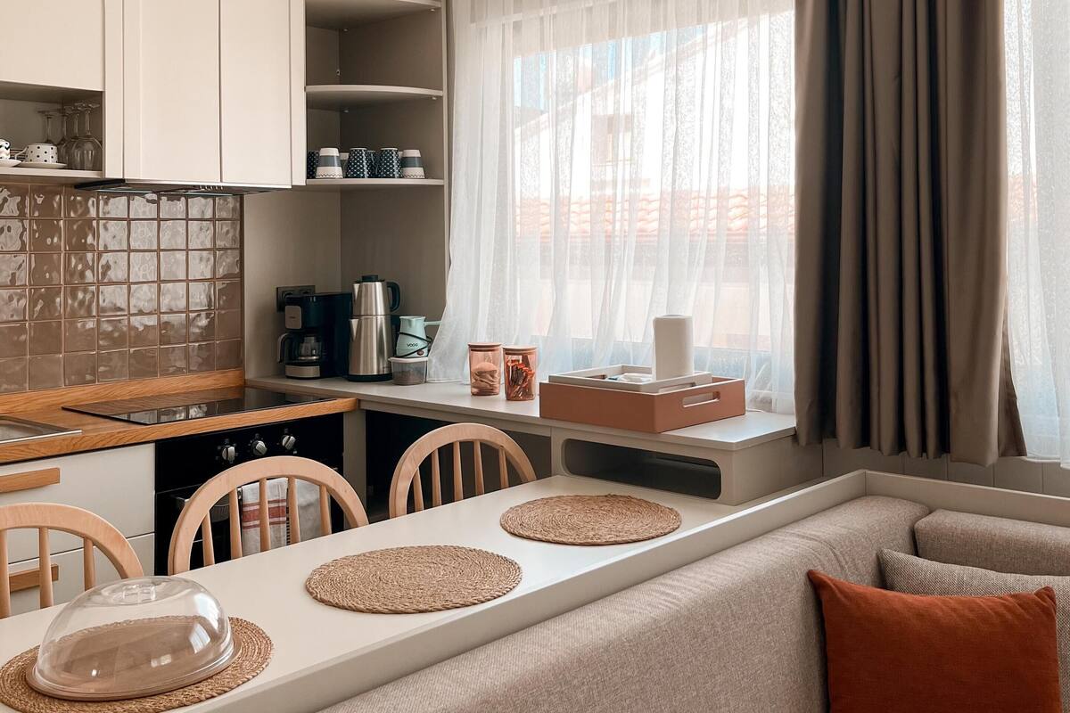 Eine moderne Küche mit Essbereich, ausgestattet mit Backofen, Kaffeemaschine und einem Esstisch mit Stühlen.