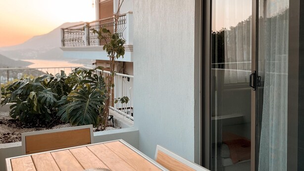 A wooden table with chairs and a glass door on a balcony overlooking a mountain. - Katana Suites Kaş (Kas)