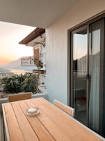 Una mesa de madera con sillas y un vidrio en un balcón con vista a una montaña.