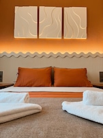 Habitación de hotel con cama, dos almohadas, cabecero con diseño de olas y lámpara fijada a la pared.