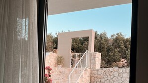 A balcony with two wooden chairs and a small table, overlooking a stone wall and a staircase leading to an upper level. - Katana Suites Kaş (Kas)