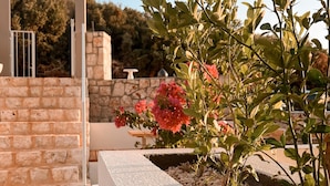 A modern outdoor area with a stone wall, a white planter with pebbles, and a flowering plant. - Katana Suites Kaş (Kas)