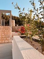 Un espacio exterior moderno con un muro de piedra, una jardinera blanca con guijarros y una planta en flor.