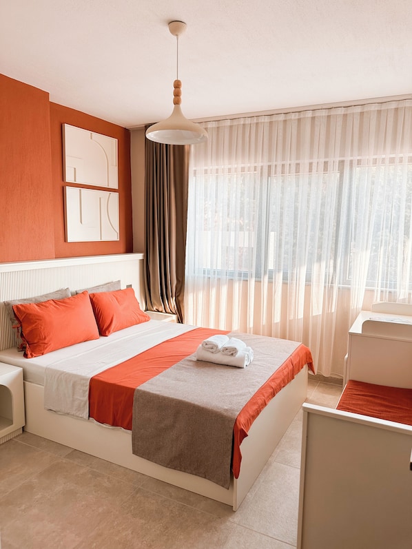 A hotel room with a bed, a desk, a chair, a window with curtains, and a ceiling light. - Katana Suites Kaş (Kas)