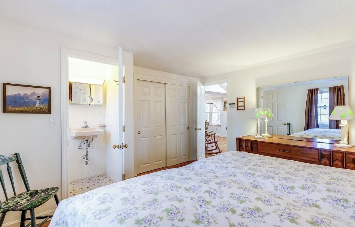 Een slaapkamer met een bed, een dressoir, een stoel, een spiegel, een deur en een raam.