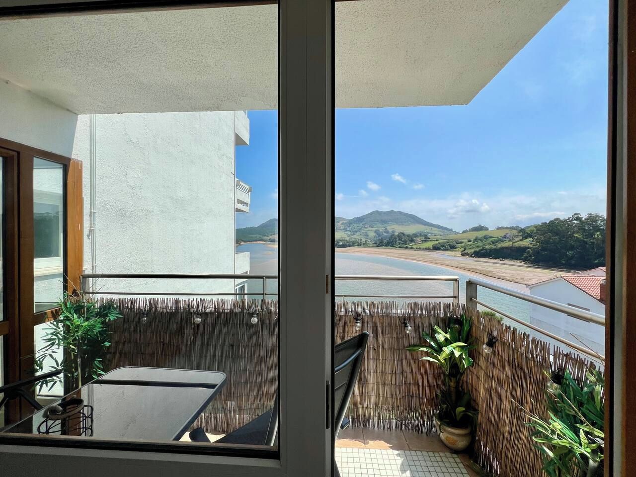 Ein Balkon mit Blick auf einen Fluss und Hügel, inklusive Tisch, Stühle und Topfpflanzen.