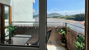 Un balcon avec vue sur une rivière et des collines, une table, des chaises et des plantes en pot.