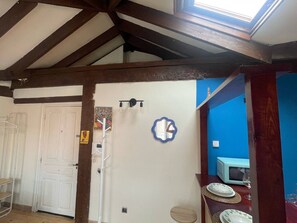 A room with a sloped ceiling, a white door, a blue wall, a microwave, and a small table with a plate and glass. - MiniLoft Cisneros - by Wehomes (Santander)