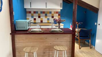 Cocina pequeña equipada con microondas, dos taburetes y una mesa para dos personas.