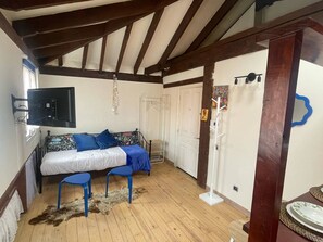 Una habitación con una cama, dos taburetes azules, un televisor y una puerta blanca.