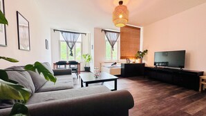 A modern living room with a sofa, dining table, TV, and large windows. - Appartementhaus am Dom  (Halle (Saale))