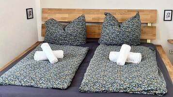 A double bed with a wooden frame, two pillows, and two rolled towels. There are two framed artworks on the wall above the bed.