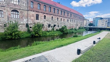 Un edificio histórico con techo rojo, un río al frente y un puente en el fondo.