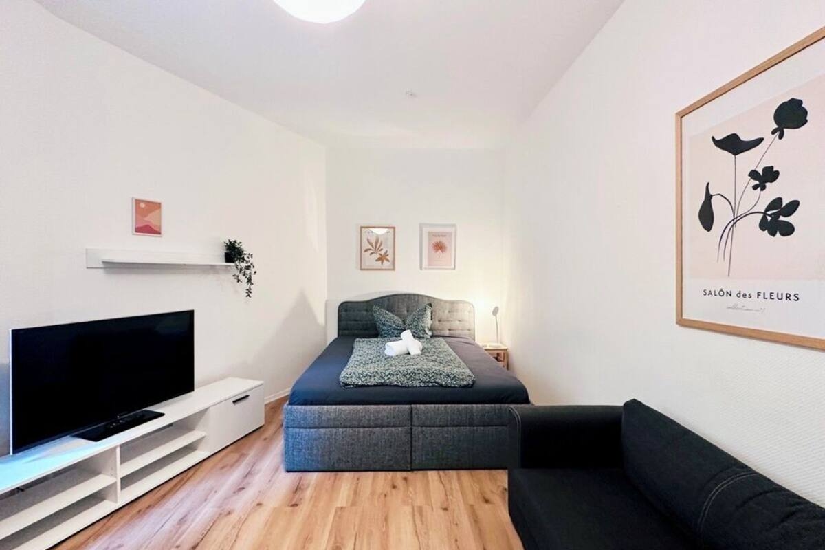 Un soggiorno moderno con televisione a schermo piatto, un divano, un letto con materasso grigio e un'opera d'arte incorniciata appesa al muro.