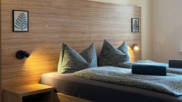 A modern bedroom with a wooden headboard, floral-patterned bedding, and two framed leaf designs on the wall.
