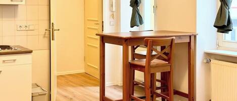 A compact kitchen with a wooden table and chair, a white cabinet, and a radiator.