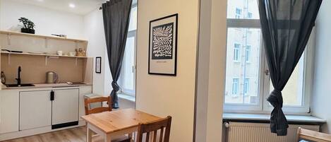 Un espacio habitable compacto con kitchenette, comedor y ventana con cortinas ligeras.