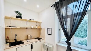 A compact kitchen with a sink, cabinets, and a window with a curtain. - Appartementhaus am Dom  (Halle (Saale))