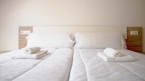 Uma cama bem arrumada com roupa de cama e toalhas brancas, cabeceira de madeira e decoração de parede simples.
