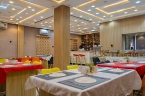 Um restaurante com mesas montadas para refeições, um bar e uma cozinha ao fundo.