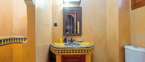 A bathroom with a yellow tiled wall, a sink with a decorative tile pattern, a mirror, and a white toilet.