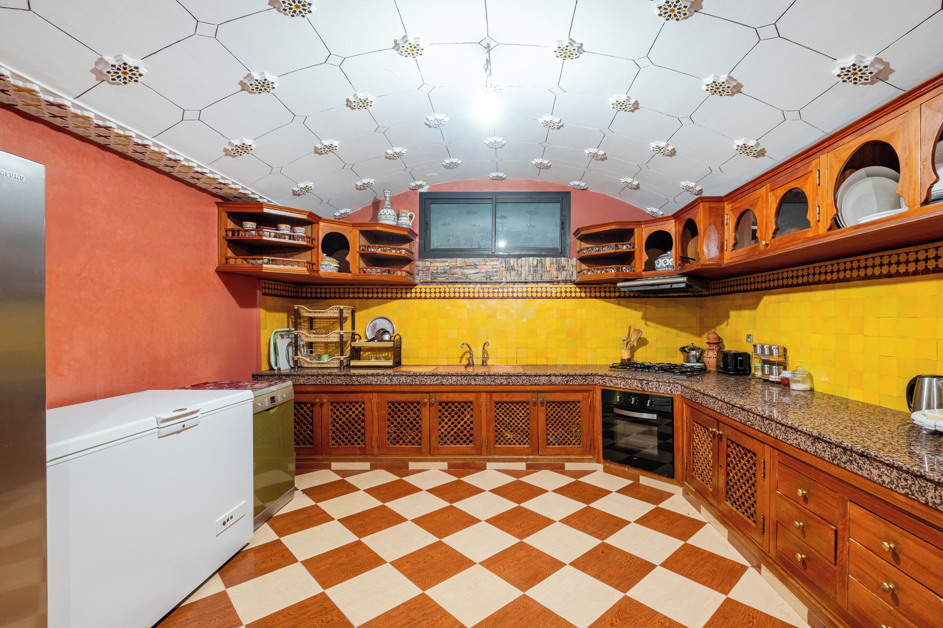Une cuisine avec un carrelage à motifs, des placards en bois, un four encastré et une fenêtre au-dessus de l’évier.