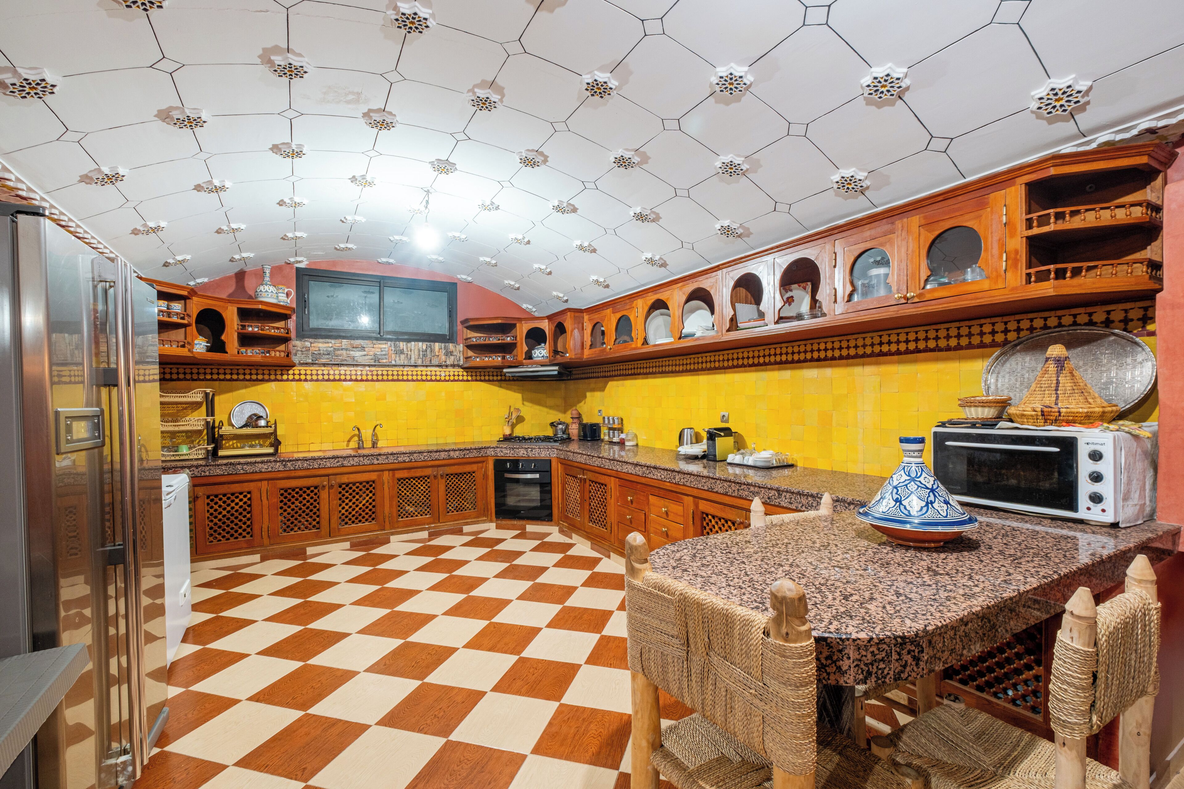 A kitchen with a checkered floor, wooden cabinets, a microwave, and a traditional Moroccan tagine.