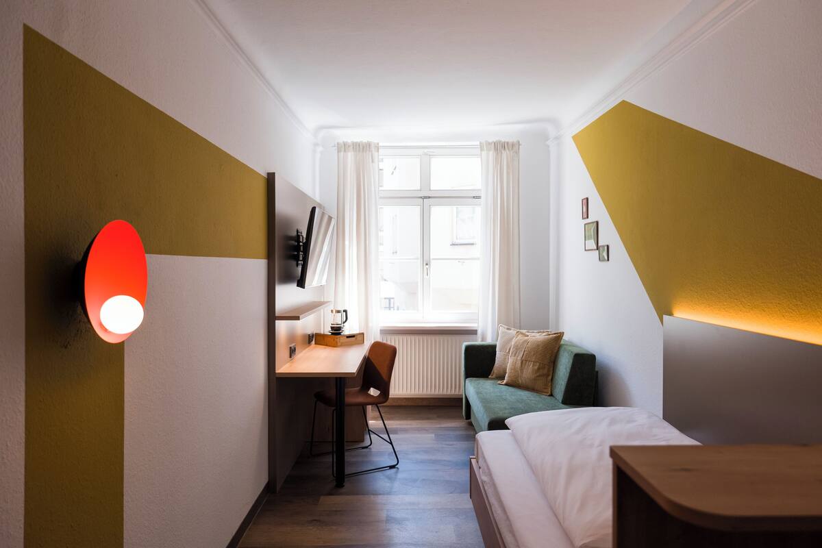 Una habitación de hotel con escritorio, sofá verde, cama y ventana con cortinas.