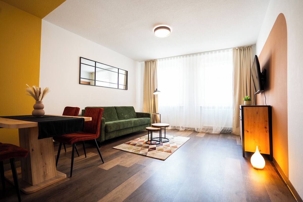 Una sala de estar con un sofá, una mesa de comedor y un televisor montado en la pared.