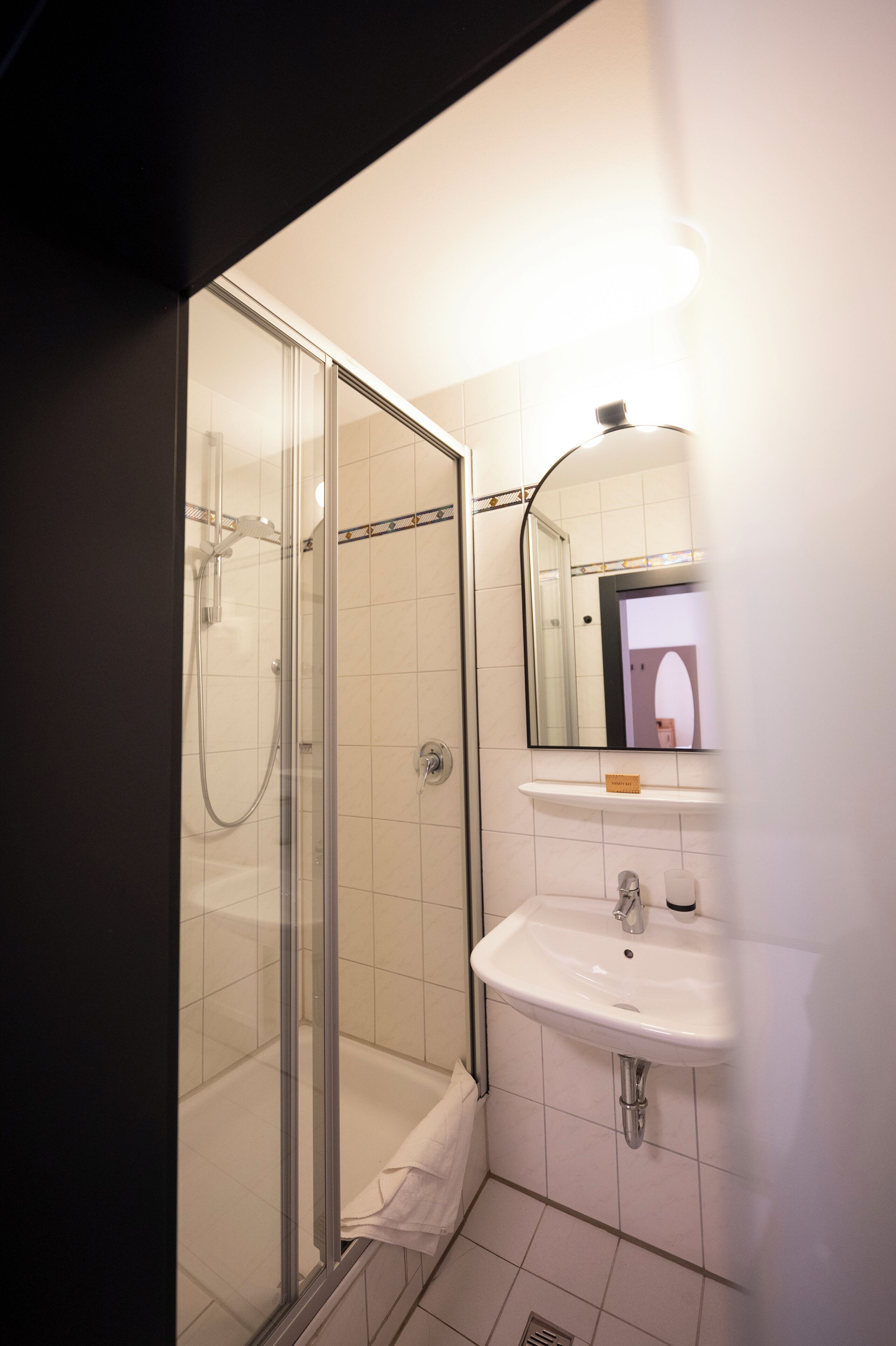 Un baño moderno con cabina de ducha acristalada, un lavabo blanco y un espejo encima.