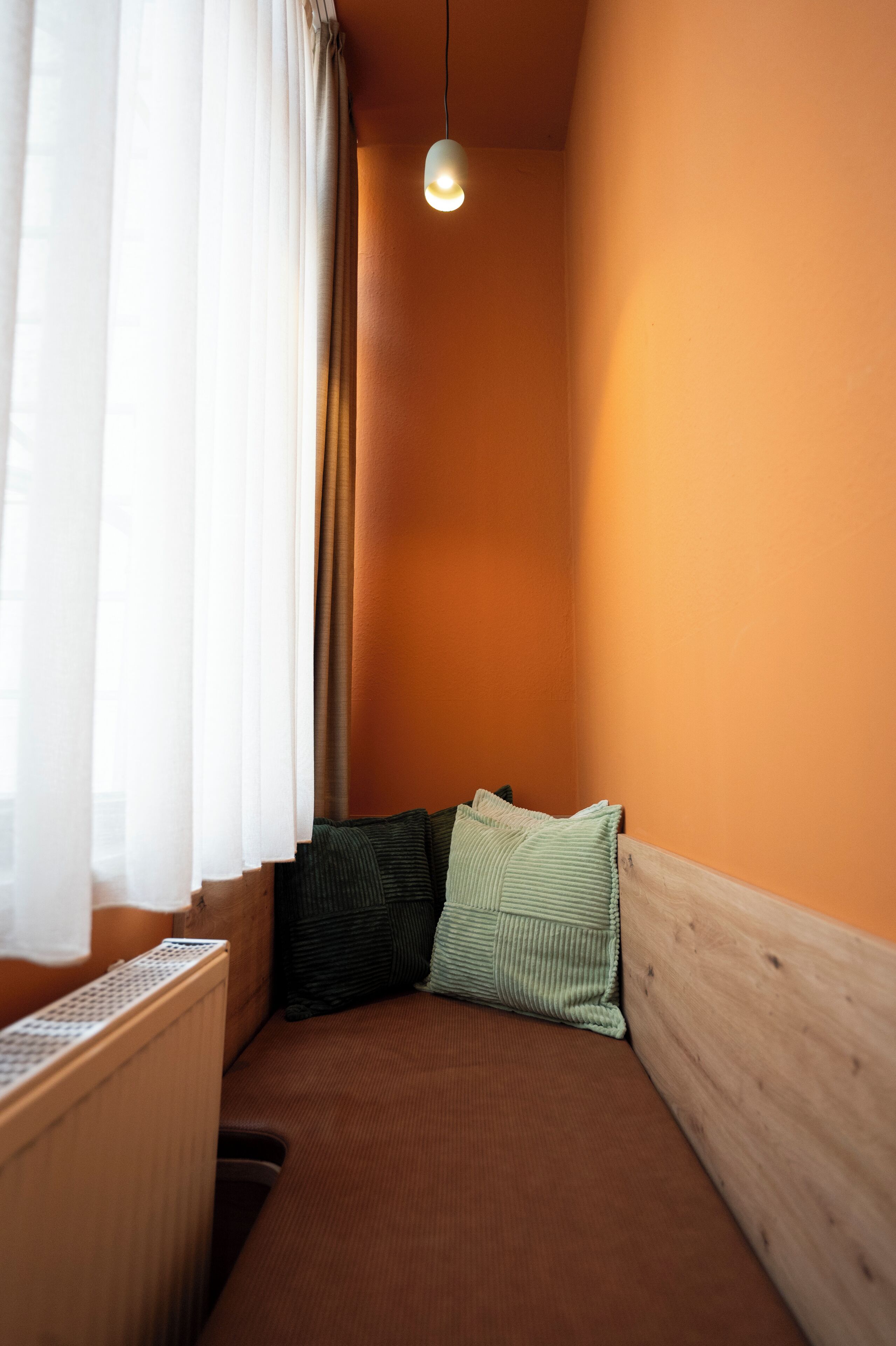 A small, cozy room with a wooden headboard, a single light fixture, and a window with sheer curtains.
