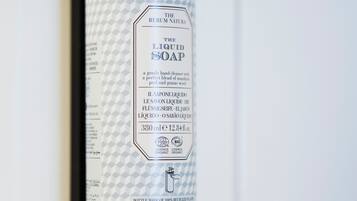 A bottle of liquid soap with a pump dispenser, labeled as organic and made from recycled materials, mounted on a white wall.