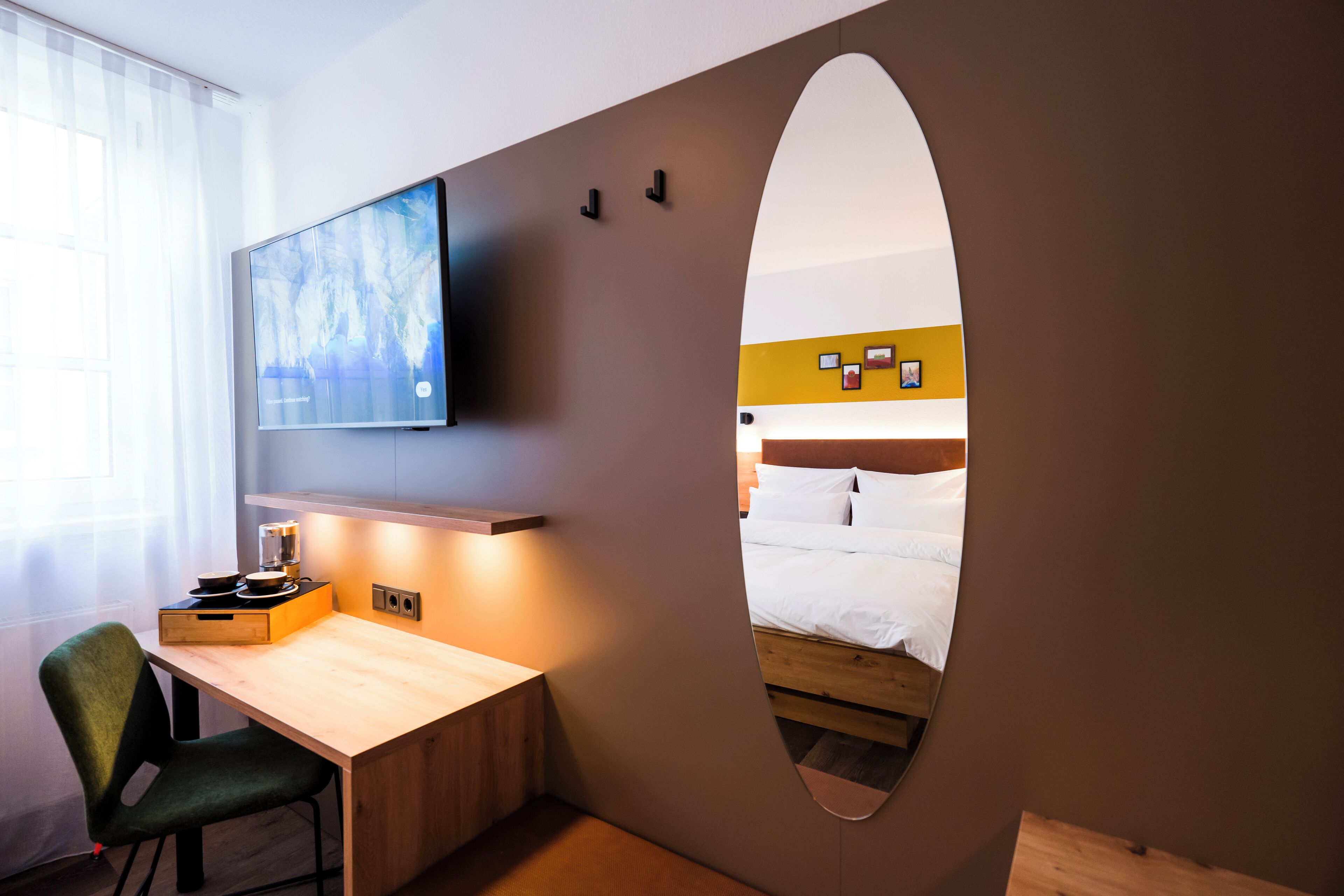 Ein Hotelzimmer mit einem Holztisch, einem grünen Sessel, einem an der Wand befestigten Flachbildfernseher und einem Bett mit weißer Bettwäsche.
