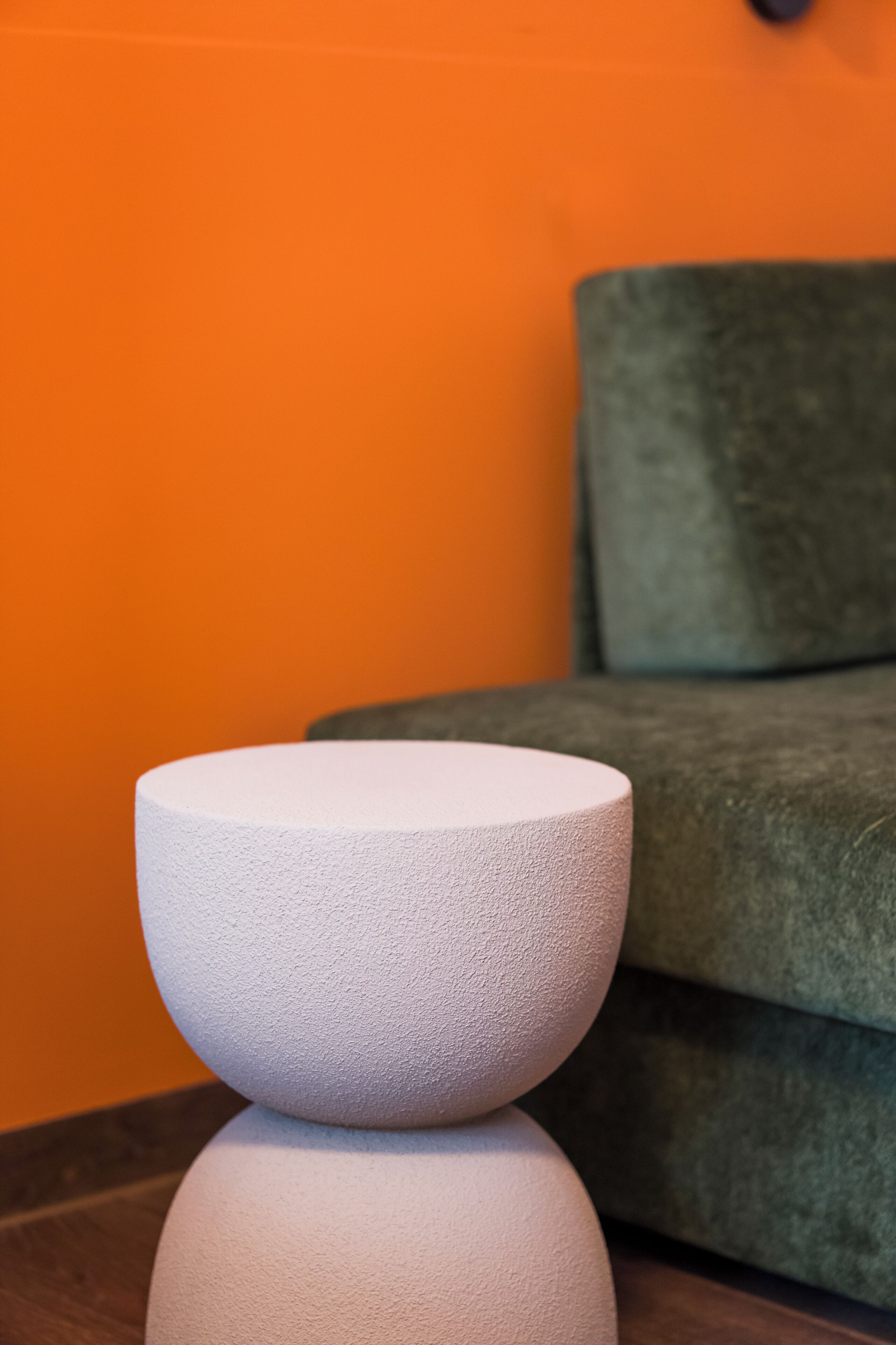 A white, textured, round object on a dark surface, possibly a table or stand, in a room with an orange wall and a green couch in the background.