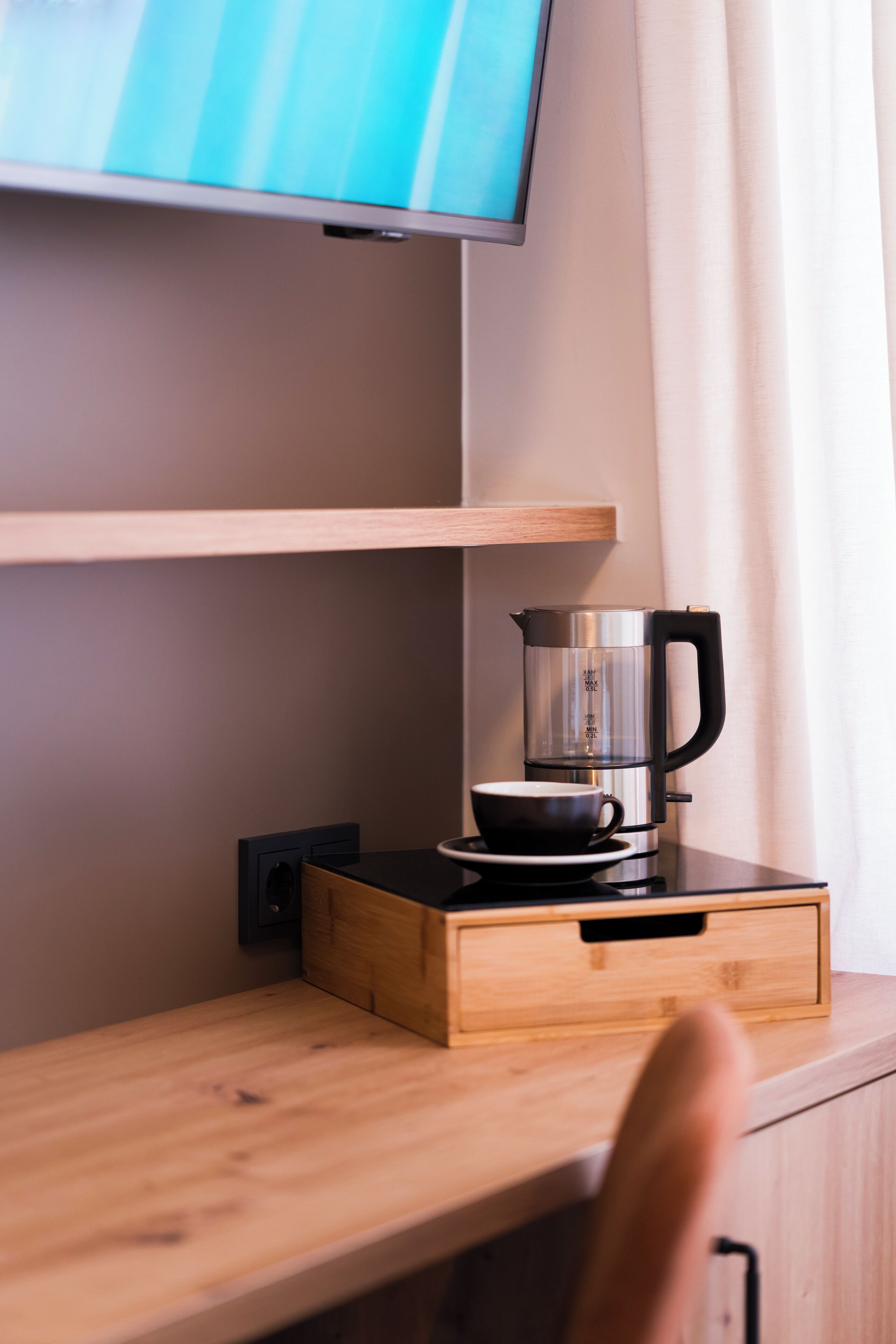 Un escritorio de madera con una cafetera, una taza y un televisor montado en la pared.