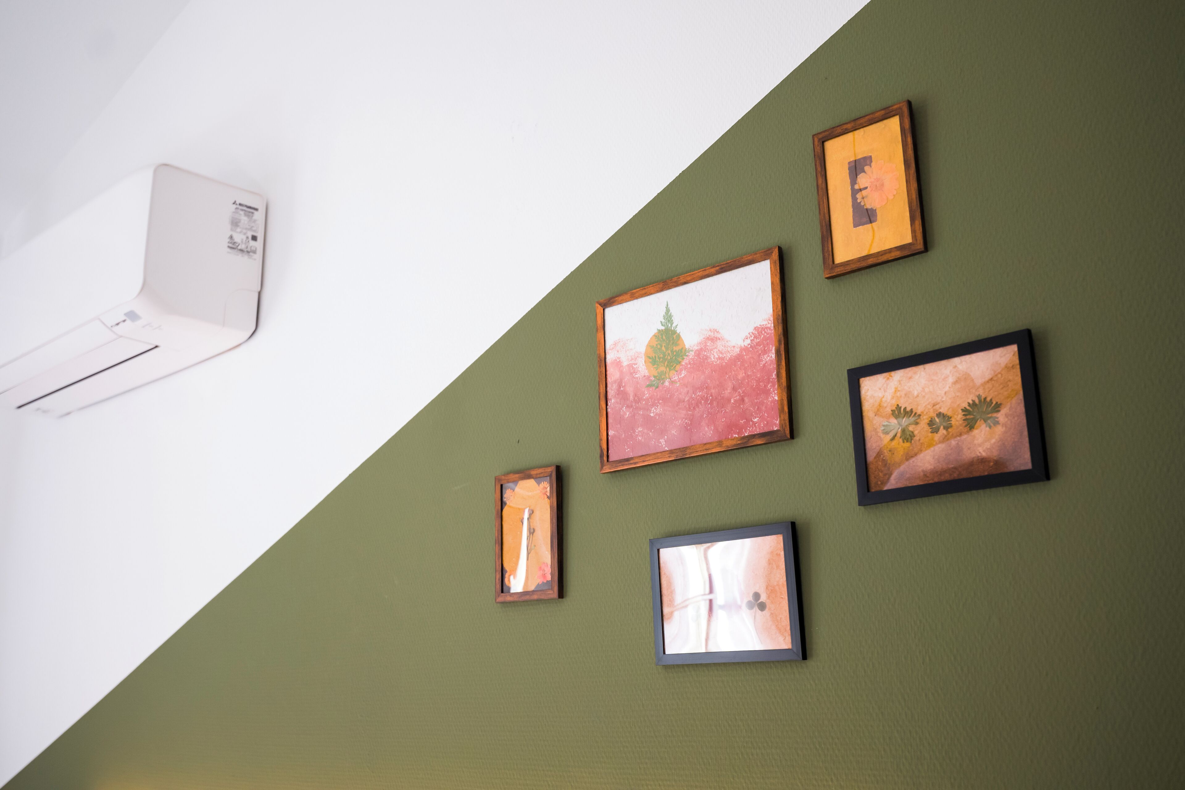 A room with a sloped ceiling, a mounted air conditioning unit, and four framed artworks on the wall.