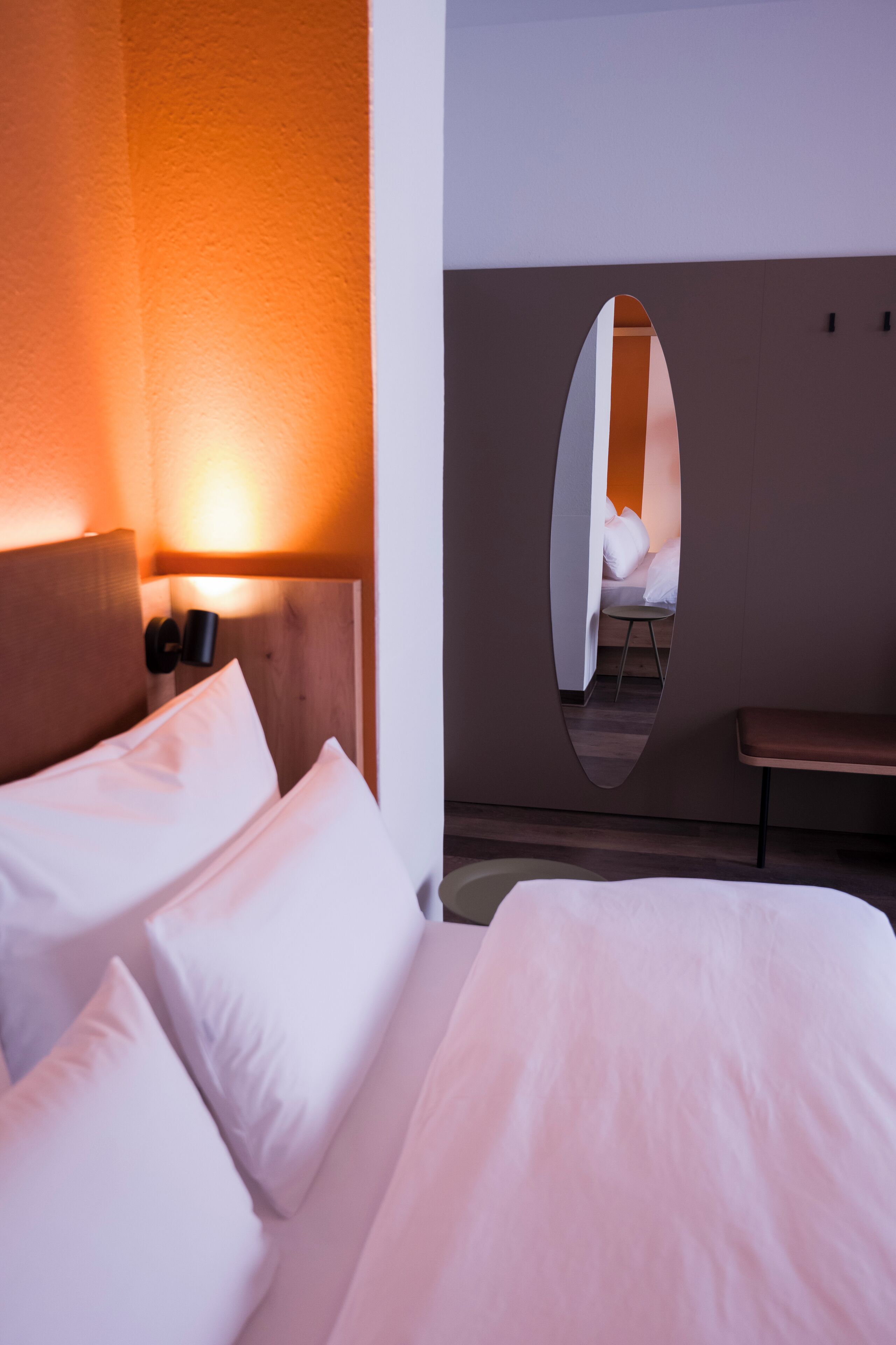 Quarto de hotel com cama, mesa de cabeceira, espelho fixado na parede e uma pequena mesa.